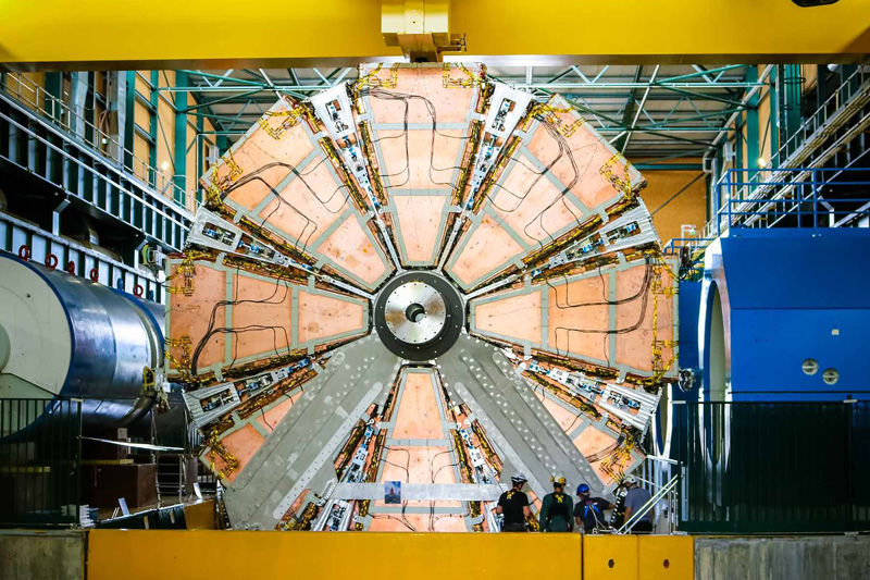 The ATLAS experiment, a wheel-shaped structure with copper wedge-shaped panels, surrounded by instrumentation. Image credit: Katarina Anthony, Copyright CERN