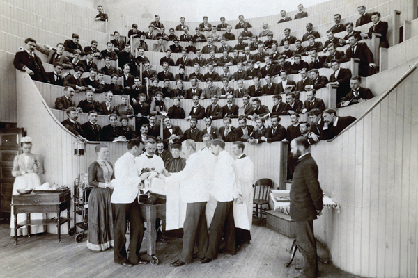 A late 19th or early 20th century photo of an amphitheater with students observing a medical demostration on the floor below
