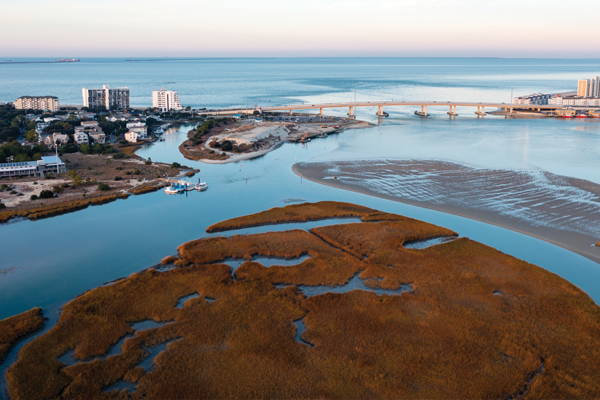 Aerial view of a coastal community at dusk showing brown marshlands in the foreground