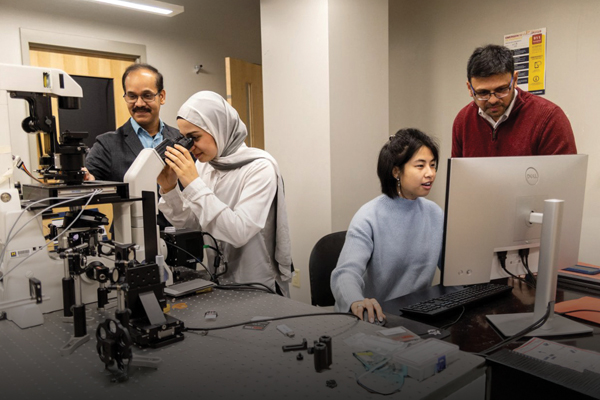 Young researchers working on a telescope and a computer while mentor faculty look on