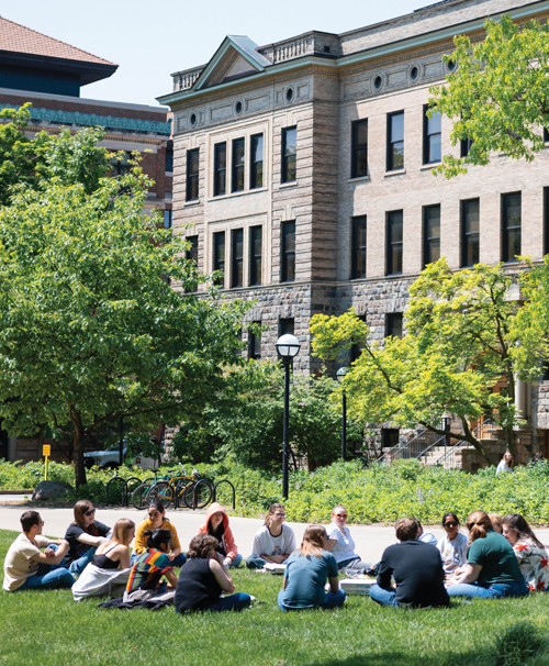 Students sitting in a circle on the lawn outside of the Dana Building